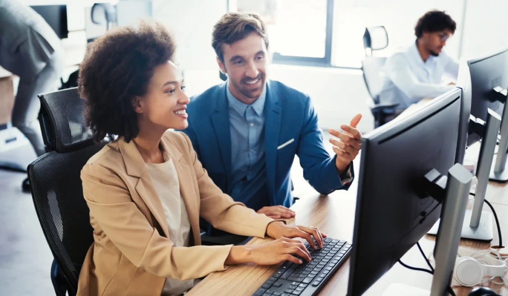 Business professionals collaborating at a computer, discussing cybersecurity solutions for business protection.