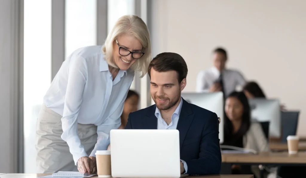 Businesswoman assisting a colleague with cybersecurity measures on a laptop in an office setting.